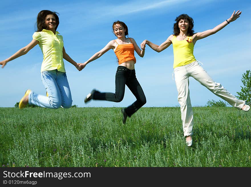 Three girlfriend jump in green field under blue sky