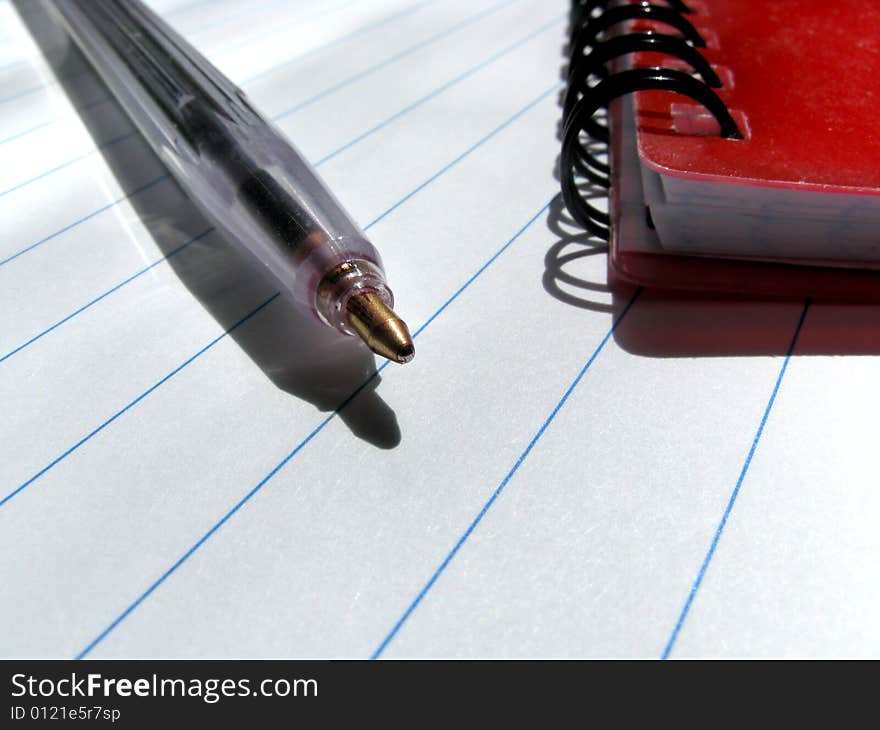 Ballpen and a notebook on a lined surface of a writing-book. Ballpen and a notebook on a lined surface of a writing-book