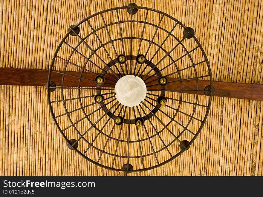 An iron light fixture hanging from a bamboo roof. An iron light fixture hanging from a bamboo roof