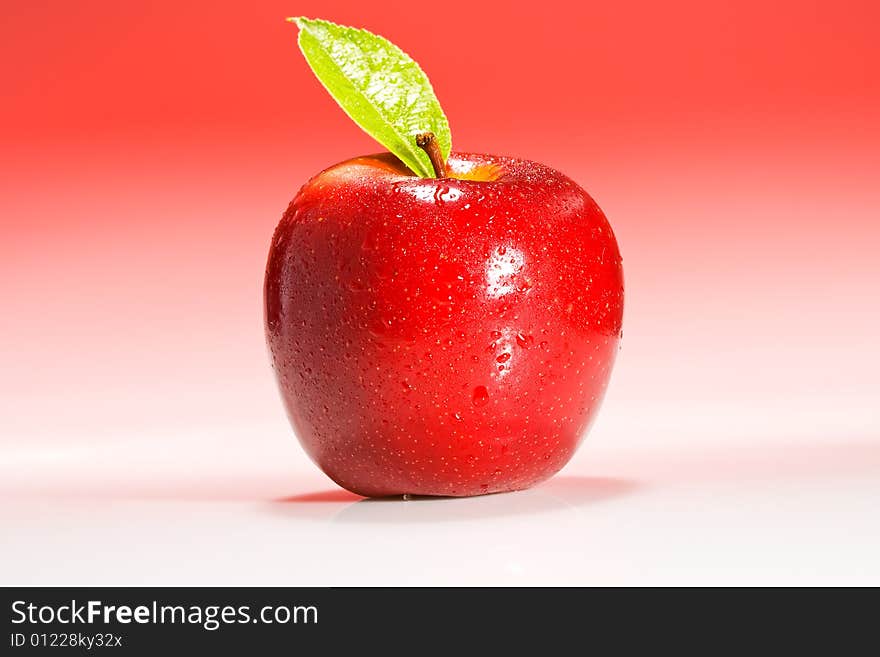 Red Shinny Apple with water drops and a green leaf on a red gradient background. Red Shinny Apple with water drops and a green leaf on a red gradient background