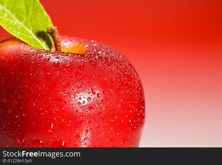 Red Shinny Apple with water drops and a green leaf on a red gradient background. Red Shinny Apple with water drops and a green leaf on a red gradient background