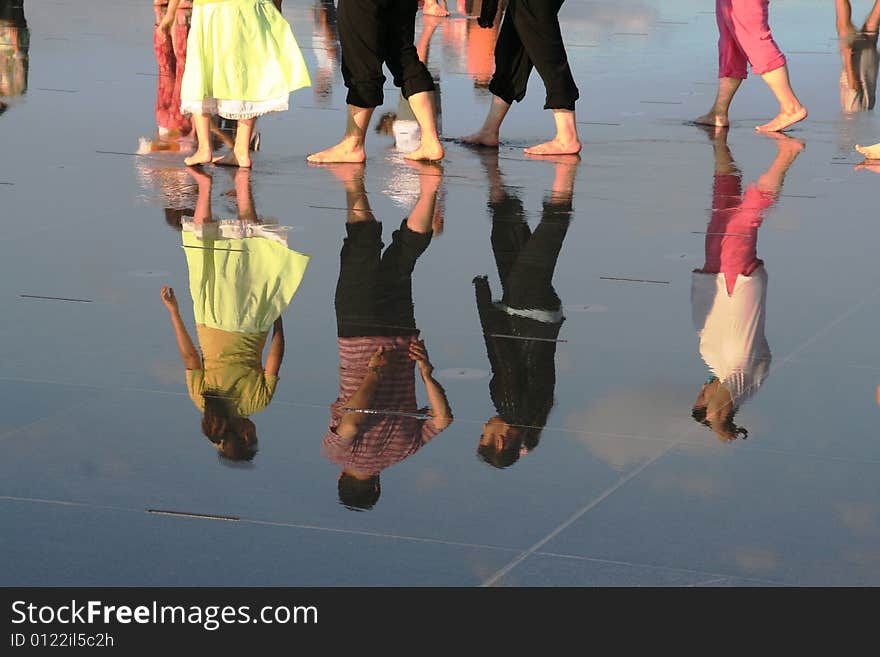 People walking barfoot in a big reflective puddle. People walking barfoot in a big reflective puddle