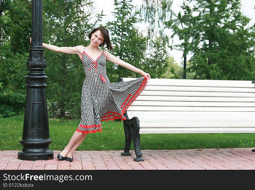 The beautiful girl poses at a lamppost and a bench