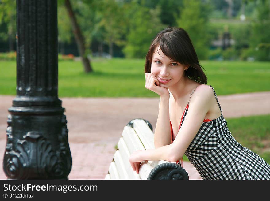 The beautiful girl poses at a lamppost and a bench