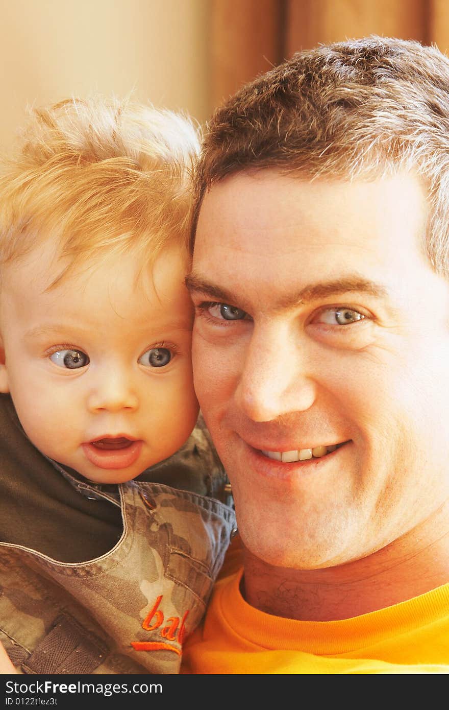 Man holding baby boy close, cheek to cheeck, looking at camera with smile, focus on baby. Man holding baby boy close, cheek to cheeck, looking at camera with smile, focus on baby