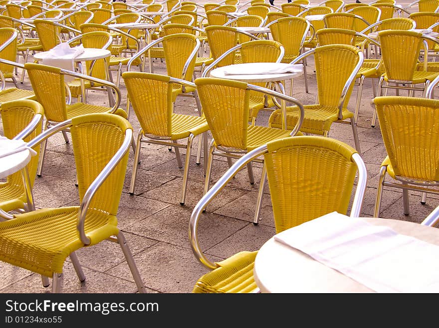 A terrace with yellow chairs and round tables