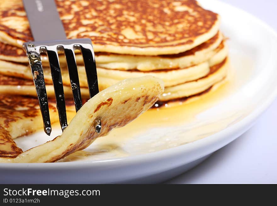 Pile of american pancakes with syrup on a dish and fork piercing a piece. Pile of american pancakes with syrup on a dish and fork piercing a piece.