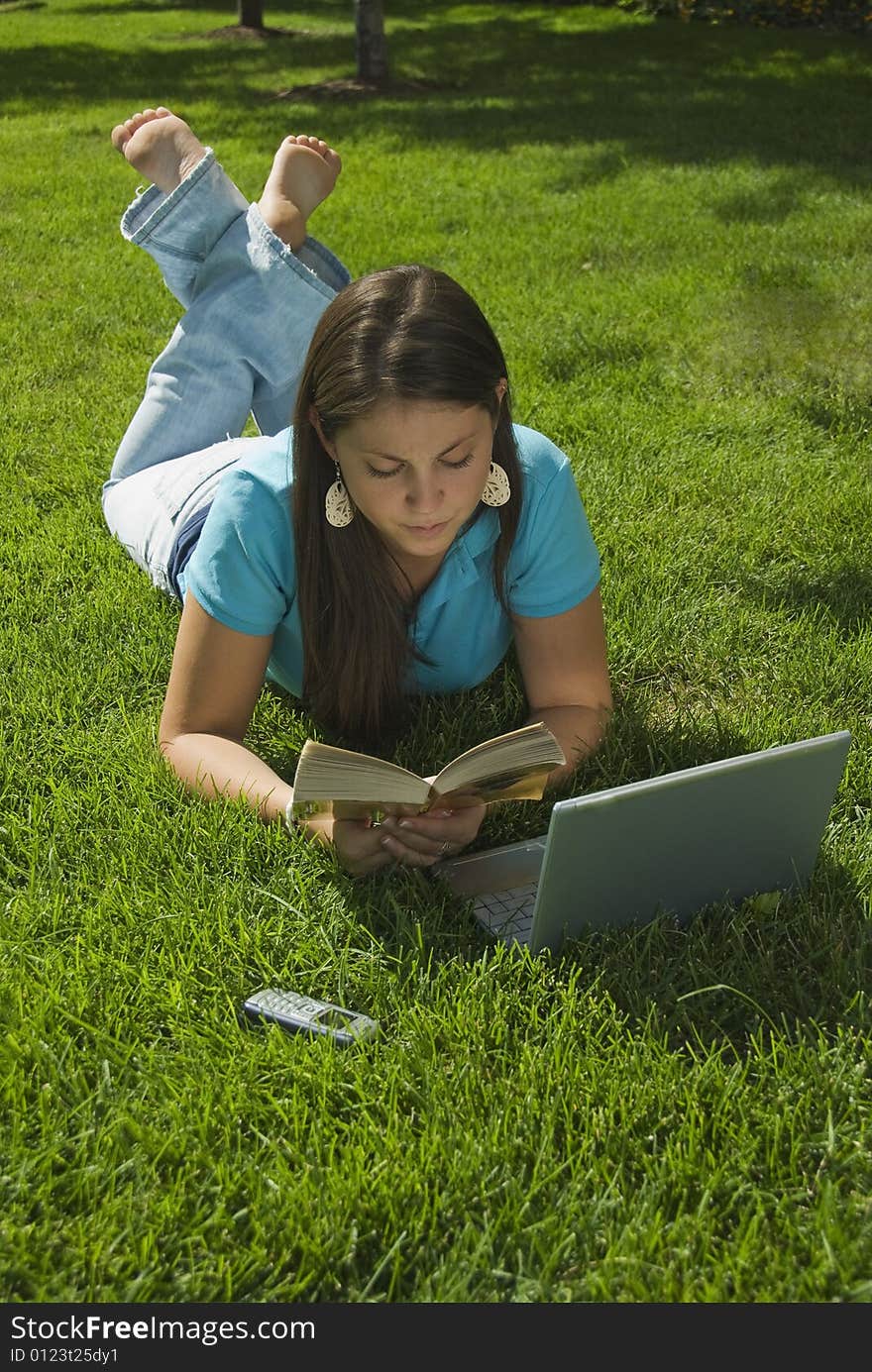 Girl in grass with computer, book, and cell phone. Girl in grass with computer, book, and cell phone