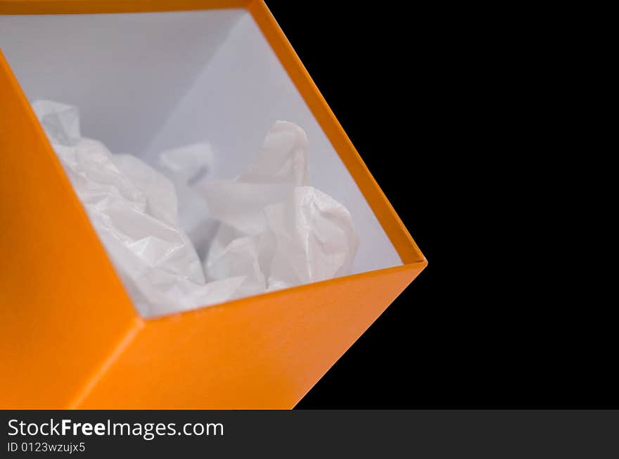 Close up of orange opened box with white paper on black background