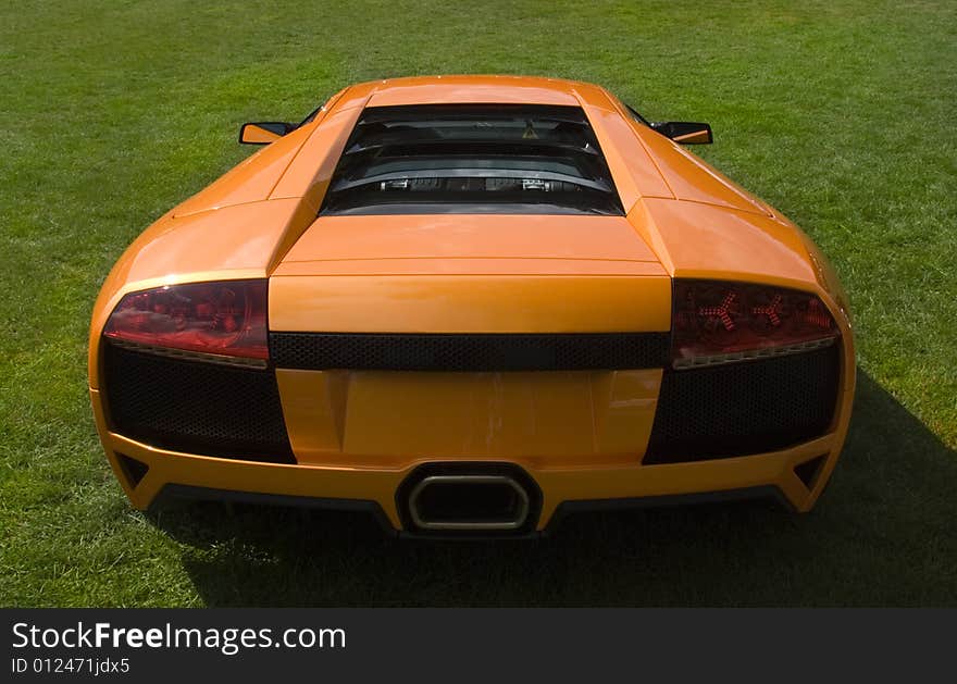 Rear end of Italian super car in metallic orange on lawn. Rear end of Italian super car in metallic orange on lawn