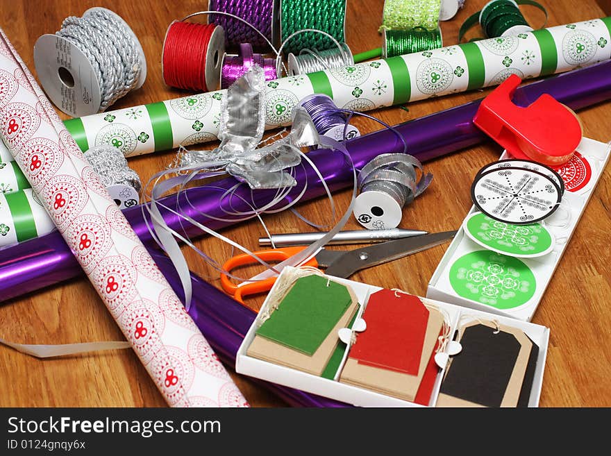 A bunch of wrapping paper, ribbons, label tags and other present wrapping material on an oak table