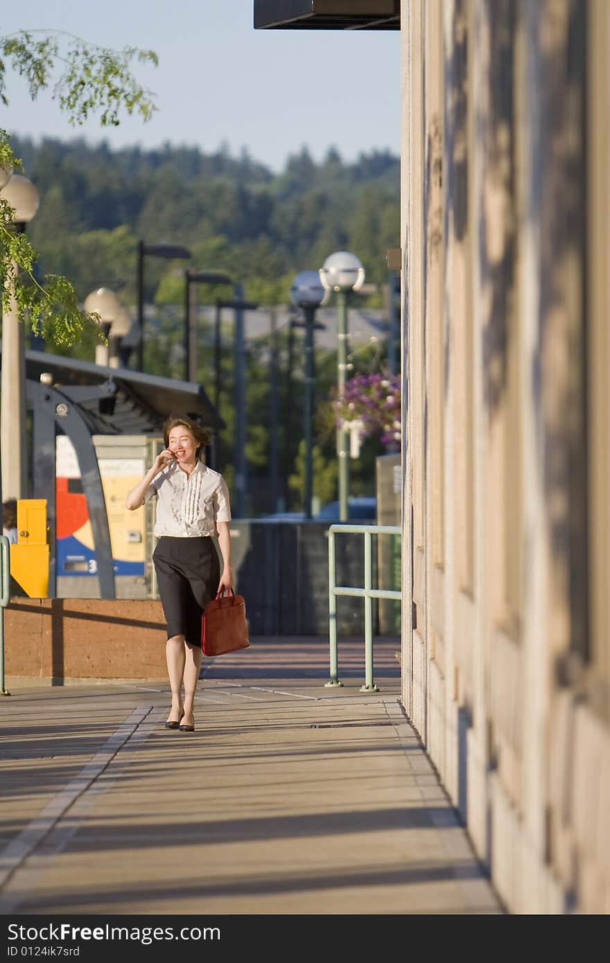 Young woman walks along building while talking on cell phone. Vertically framed photo. Young woman walks along building while talking on cell phone. Vertically framed photo.