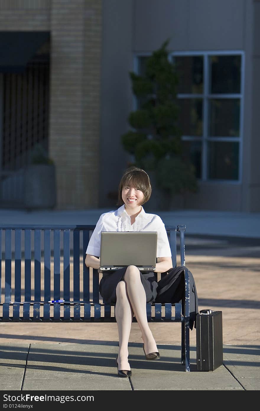 Young woman sits on a bench in front of a building. She is holding her laptop and looks surprised. Vertically framed photo. Young woman sits on a bench in front of a building. She is holding her laptop and looks surprised. Vertically framed photo.