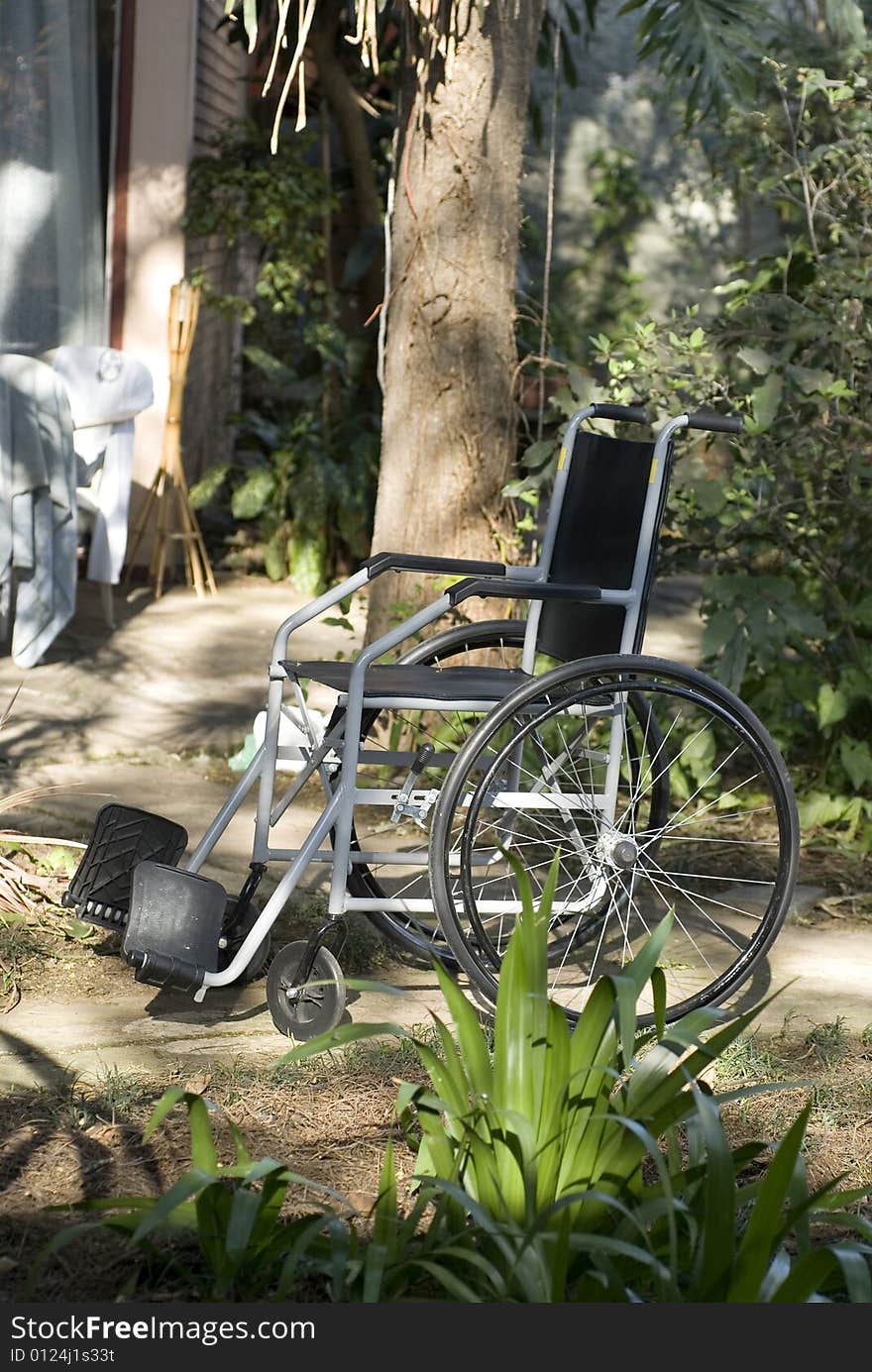 An empty wheelchair is sitting in a garden - Vertically framed shot. An empty wheelchair is sitting in a garden - Vertically framed shot