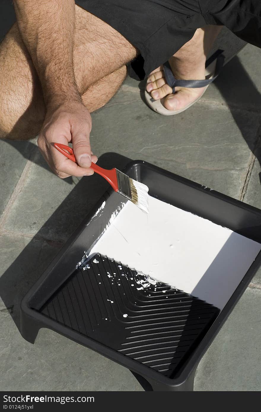 A man is dipping his paint brush into a tray of white paint - Vertically framed shot. A man is dipping his paint brush into a tray of white paint - Vertically framed shot.