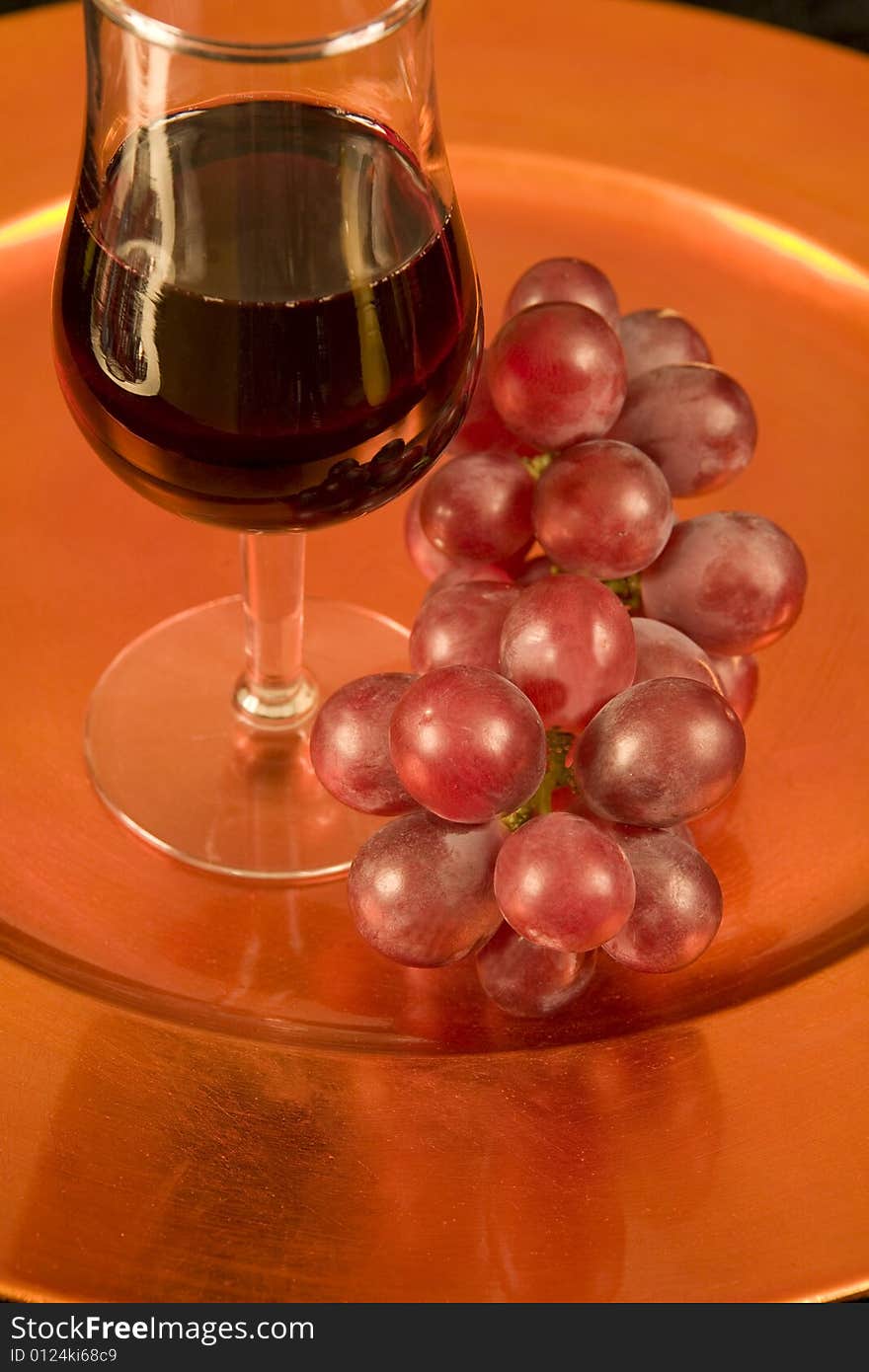 A tasting glass of red wine and grapes on a bronze tray. A tasting glass of red wine and grapes on a bronze tray.