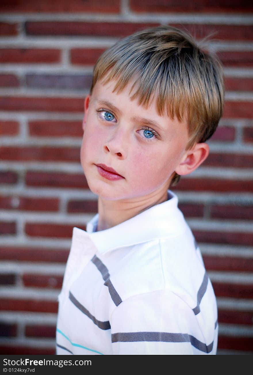 A young boy is standing up against a brick wall.  He is looking at the camera.  Vertically framed shot. A young boy is standing up against a brick wall.  He is looking at the camera.  Vertically framed shot.