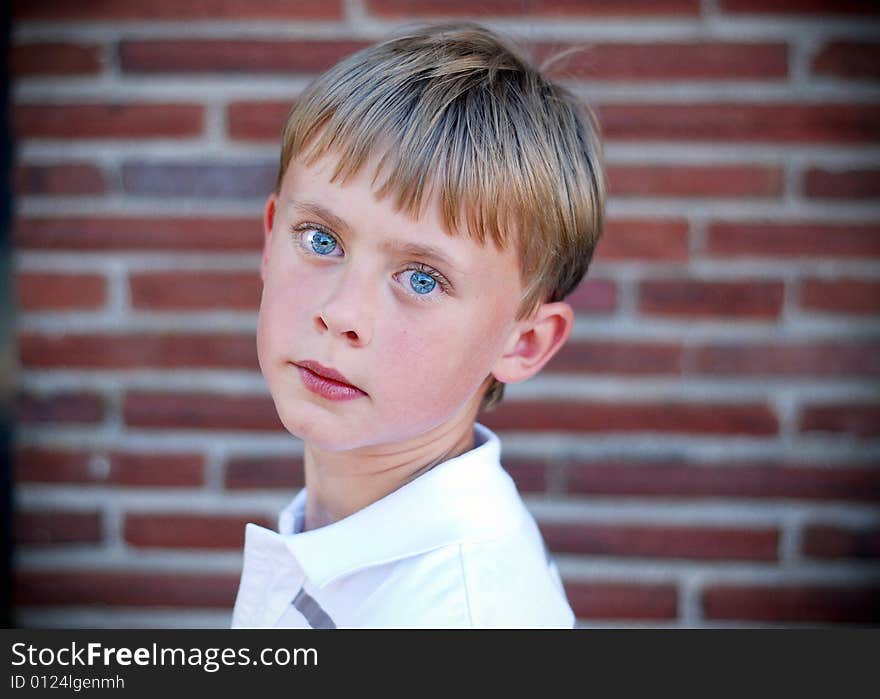 A young boy is standing up against a brick wall.  He is looking at the camera.  Horizontally framed shot. A young boy is standing up against a brick wall.  He is looking at the camera.  Horizontally framed shot.