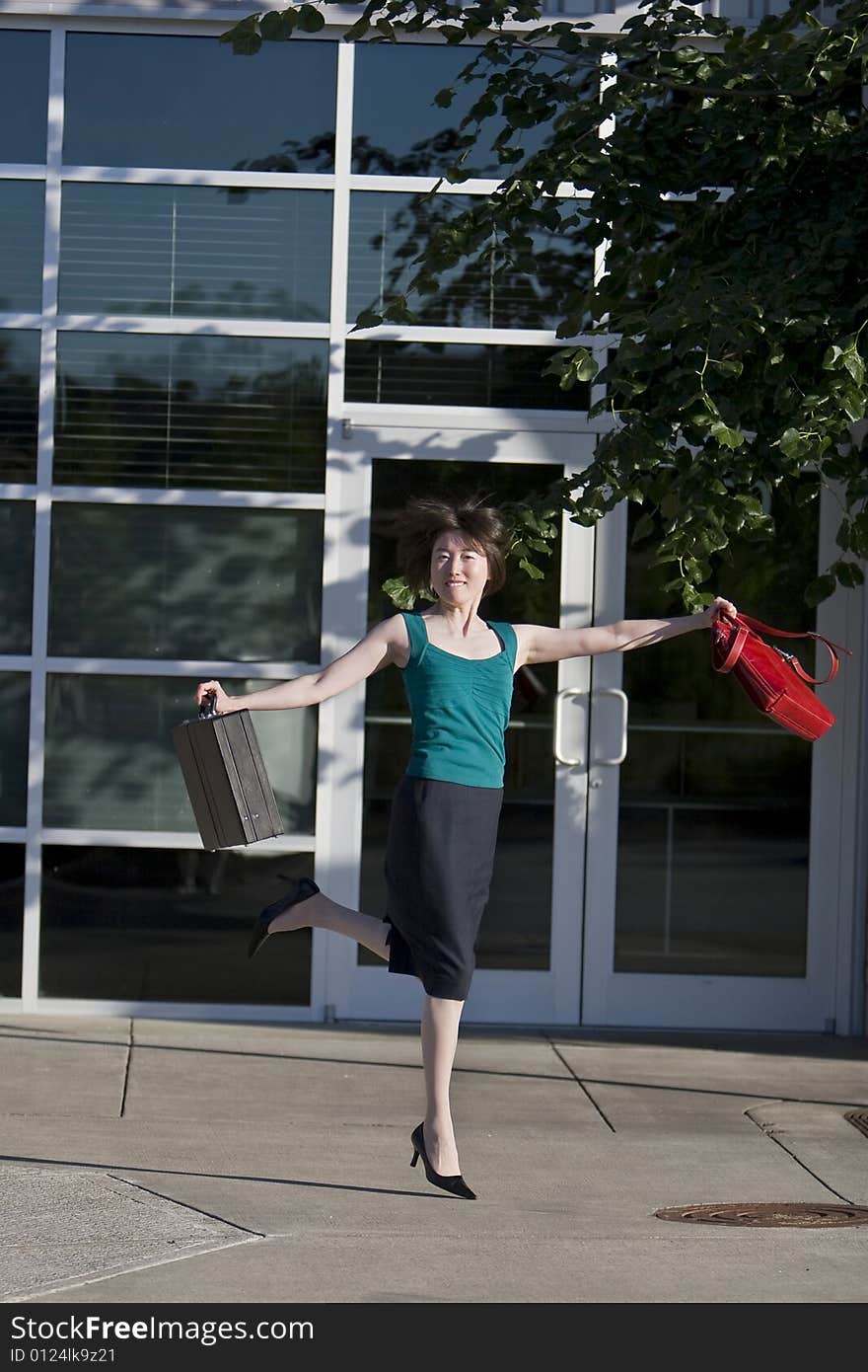 Young woman leaps in front of building while holding a red handbag and a briefcase. Vertically framed photo. Young woman leaps in front of building while holding a red handbag and a briefcase. Vertically framed photo.