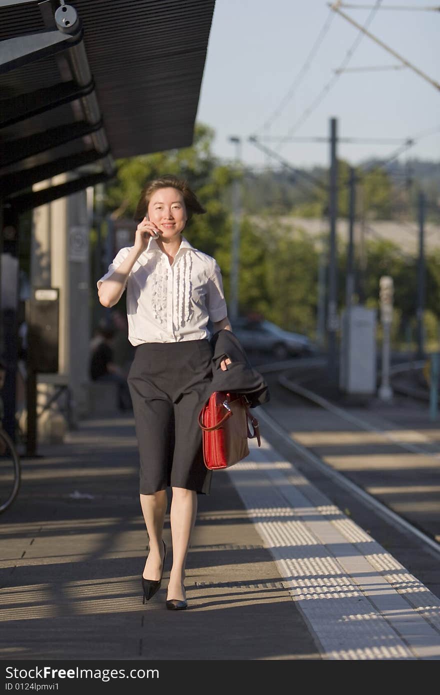 Young woman walks along tracks talking on her cell phone. She is carrying a red bag. Vertically framed photo. Young woman walks along tracks talking on her cell phone. She is carrying a red bag. Vertically framed photo.