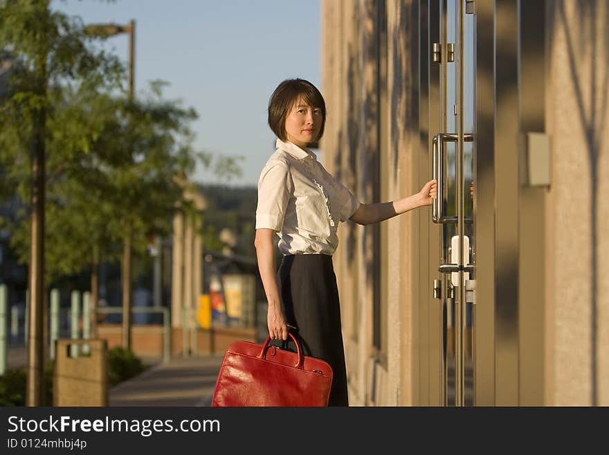 Young woman opens door while looking at the camera. She is holding a red handbag. Vertically framed photo. Young woman opens door while looking at the camera. She is holding a red handbag. Vertically framed photo.