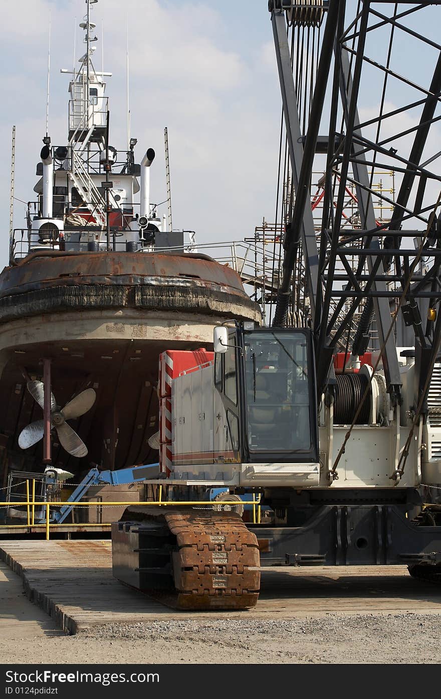 A picture of a crane and tug boat on drydock. A picture of a crane and tug boat on drydock