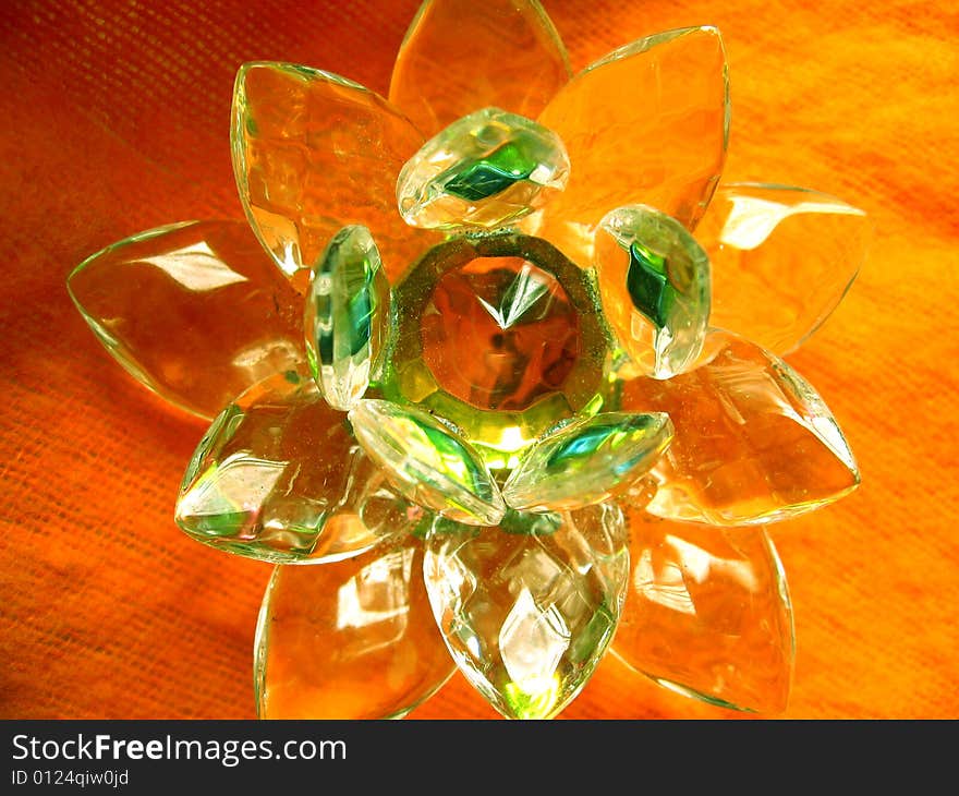 A beautiful crystal lotus showing orange colored reflection with green outline as it is kept on orange cloth