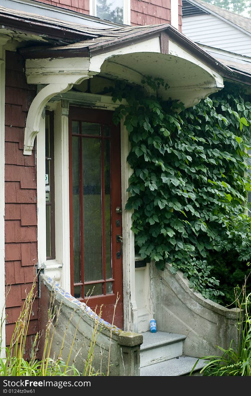 A red door covered by an awning on a shingled house. A red door covered by an awning on a shingled house.