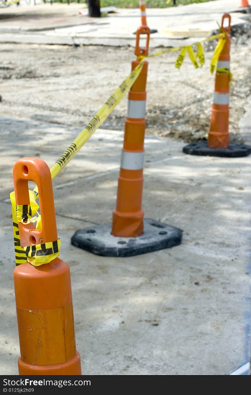 Three orange road cones bound by a yellow caution tape.