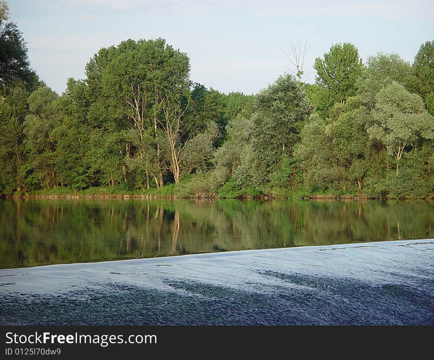 Drop into the river causing a small waterfall behind trees reflected in the calm water