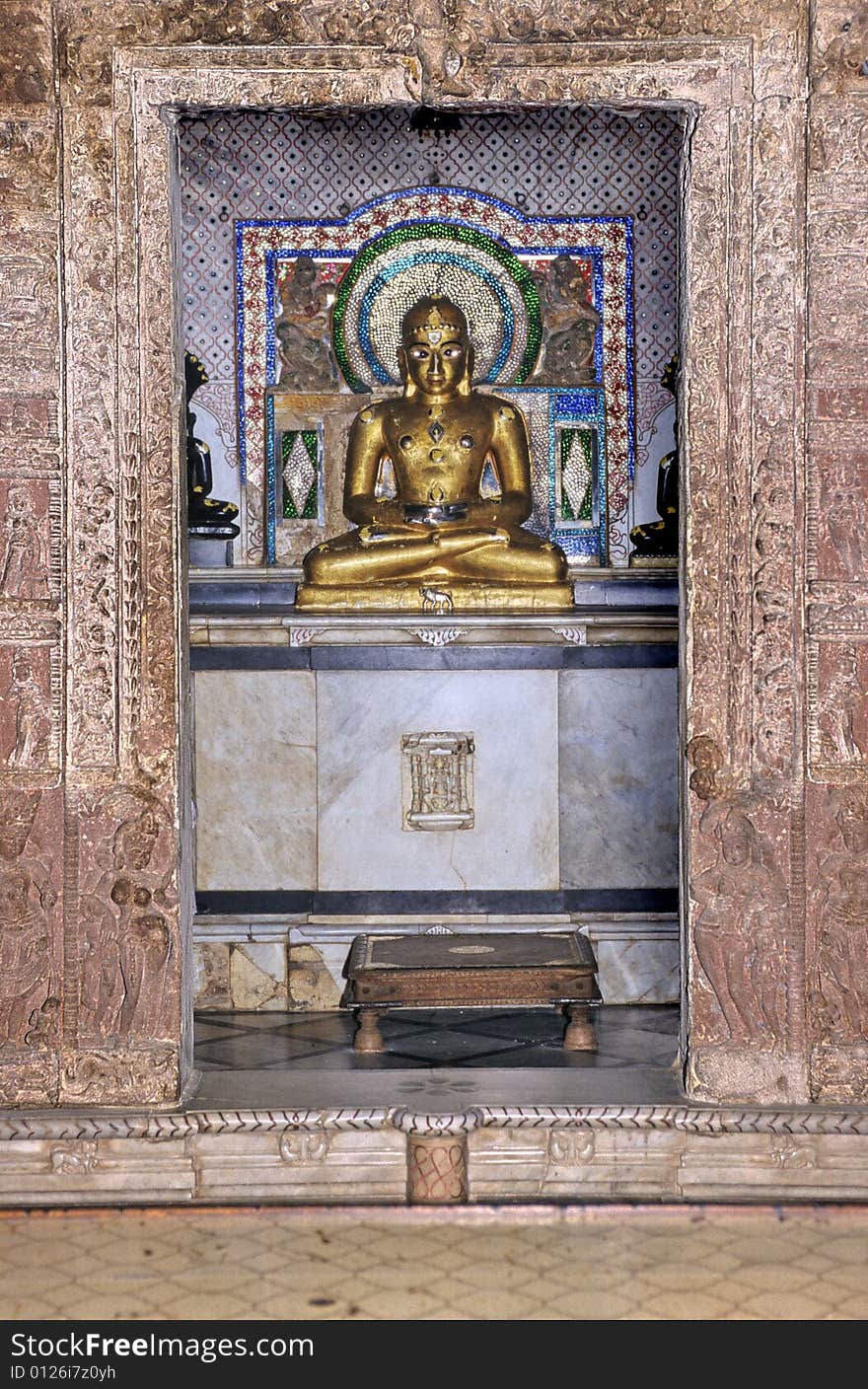 Fully carved red sandstone antechamber framing a sanctuary with a golden buddha statue of Mahavira Jain temple in Osian, near Jodhpur, Rajasthan, India. Fully carved red sandstone antechamber framing a sanctuary with a golden buddha statue of Mahavira Jain temple in Osian, near Jodhpur, Rajasthan, India.