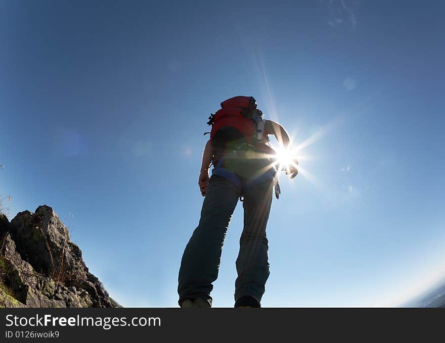 Climber, with climbing gears, standing on a stone at the top of his route, over a deep blue sky.