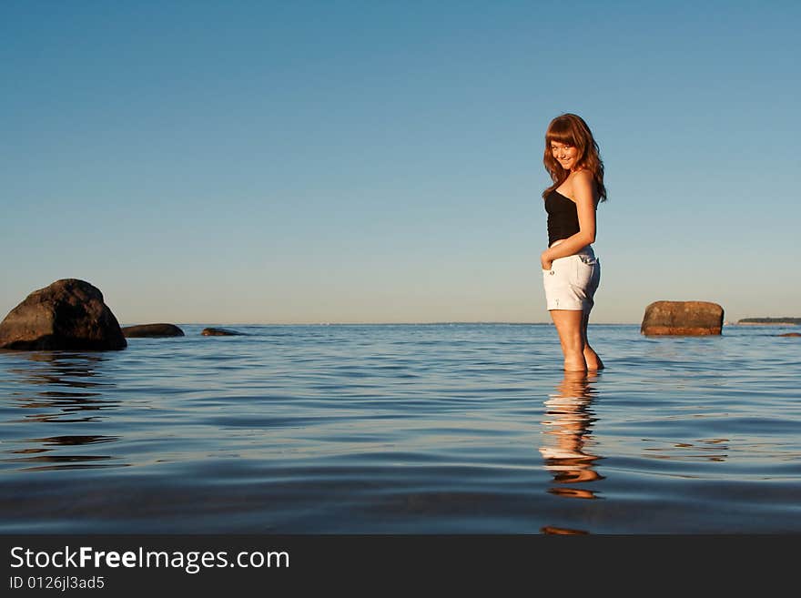 Happy young woman standing in water and looking over her shoulder