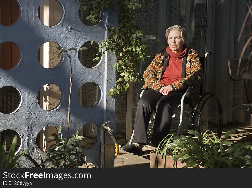 An elderly woman is sitting in a wheelchair in her garden. She is staring off into the distance. Horizontally framed shot. An elderly woman is sitting in a wheelchair in her garden. She is staring off into the distance. Horizontally framed shot.