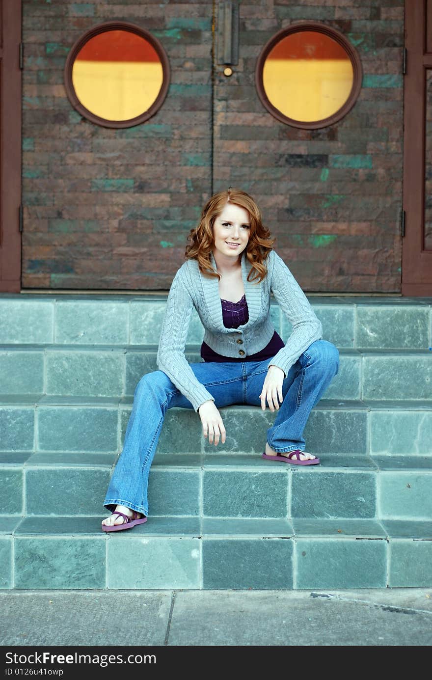 A young girl is sitting outside of a building on some stairs.  She is smiling at the camera.  Vertically framed shot. A young girl is sitting outside of a building on some stairs.  She is smiling at the camera.  Vertically framed shot.