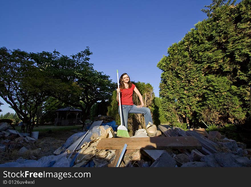 Woman standing on a pile of rubble holding a broom smiling. Horizontally framed photo. Woman standing on a pile of rubble holding a broom smiling. Horizontally framed photo.