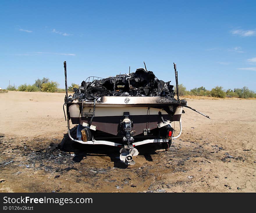 Burned wreckage of a power boat on a trailer. The boat is marooned in a desert, far from water. Horizontally framed shot. Burned wreckage of a power boat on a trailer. The boat is marooned in a desert, far from water. Horizontally framed shot.