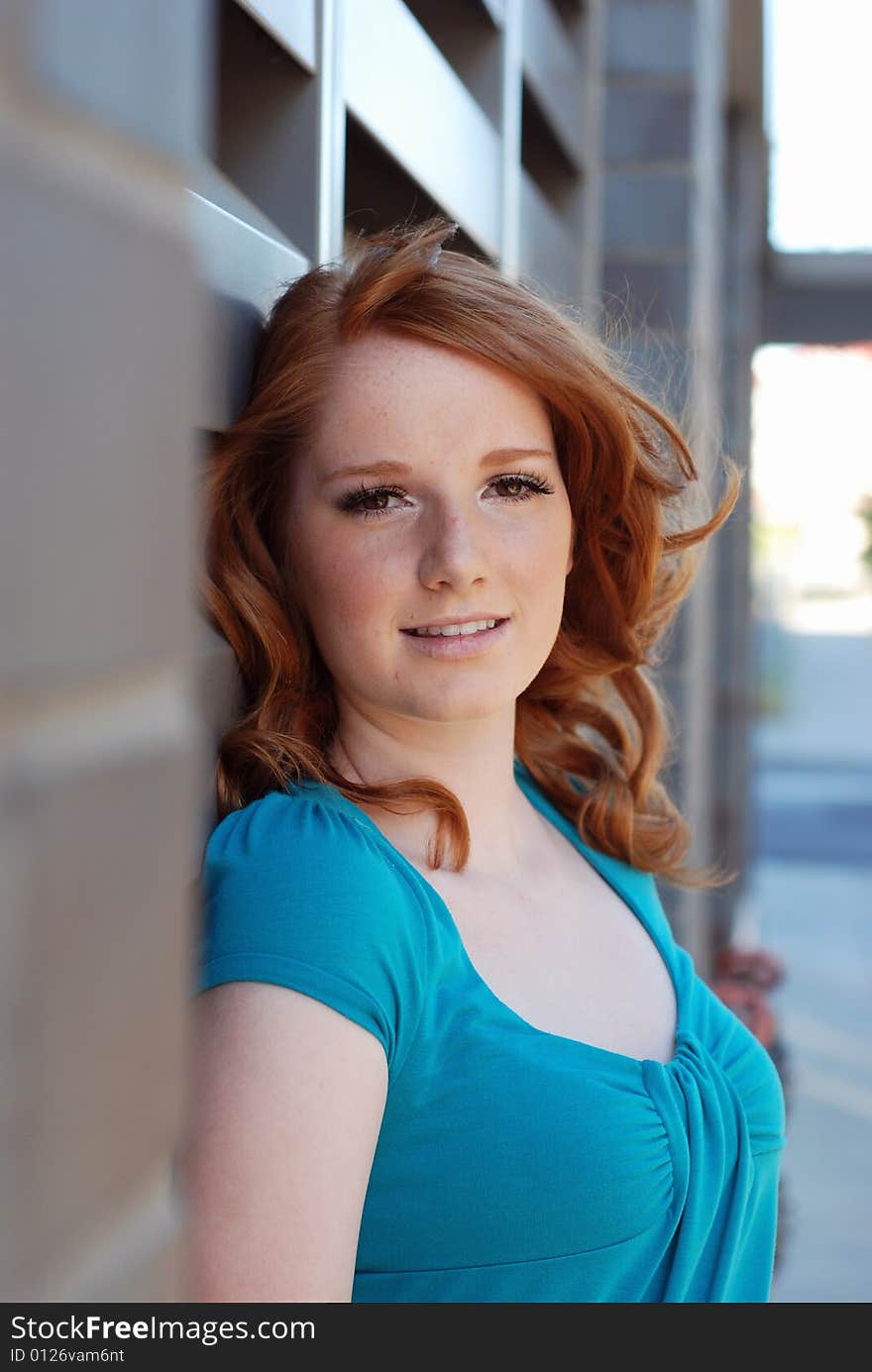 An attractive, young woman, half-smiles at the camera as she leans on a metal vent on a brick wall. Vertically framed shot. An attractive, young woman, half-smiles at the camera as she leans on a metal vent on a brick wall. Vertically framed shot.