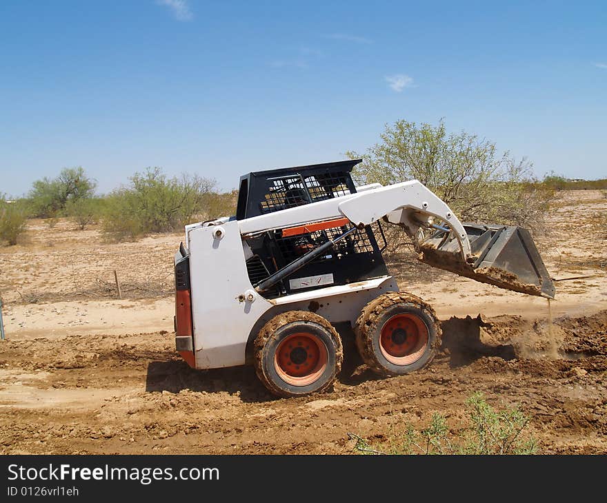 Construction worker driving a skid steer loader at a desert construction site. Horizontally framed shot. Construction worker driving a skid steer loader at a desert construction site. Horizontally framed shot.