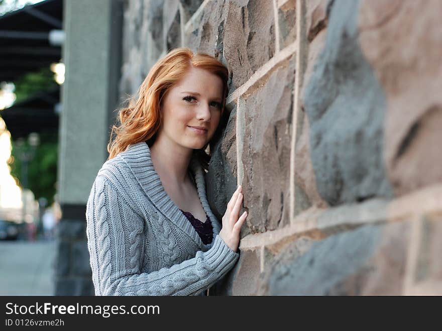 A young girl is standing next to a wall of bricks.  She is touching the wall and smiling at the camera.  Horizontally framed shot. A young girl is standing next to a wall of bricks.  She is touching the wall and smiling at the camera.  Horizontally framed shot.