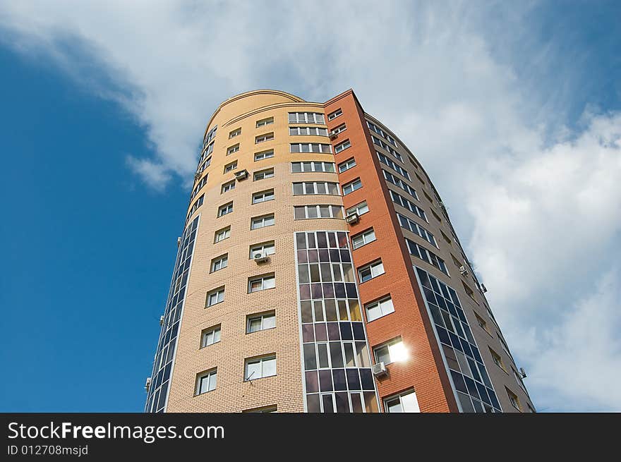 Sun glare in window of high multistory house of red and yellow bricks in blue sky