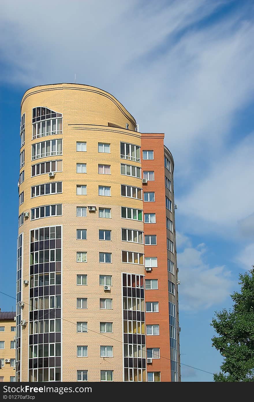 Sun glare in window of high multistory house of red and yellow bricks in blue sky