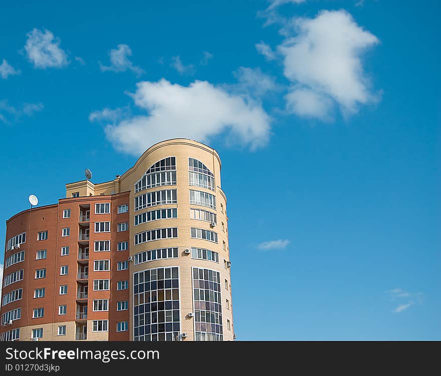 Sun glare in window of high multistory house of red and yellow bricks in blue sky