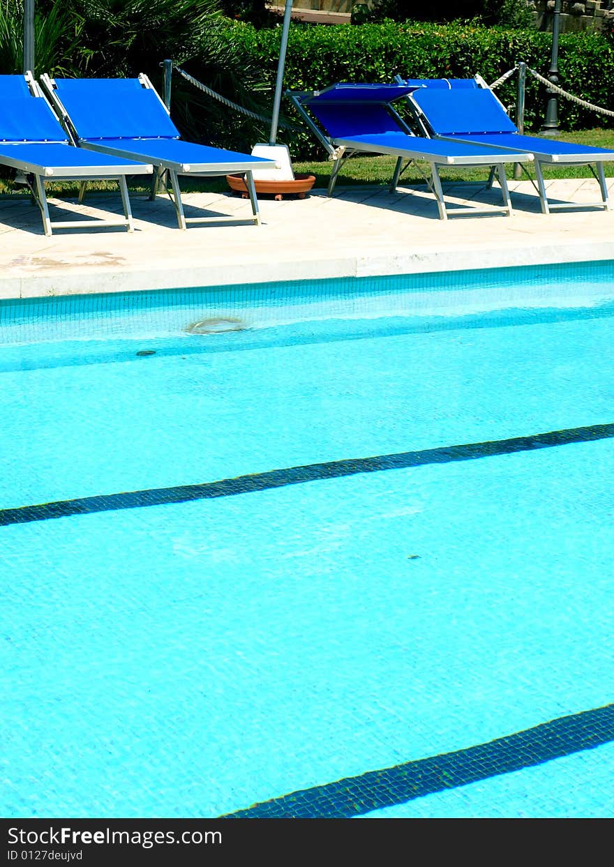 A glimpse of a pool with deck chairs and umbrella. A glimpse of a pool with deck chairs and umbrella