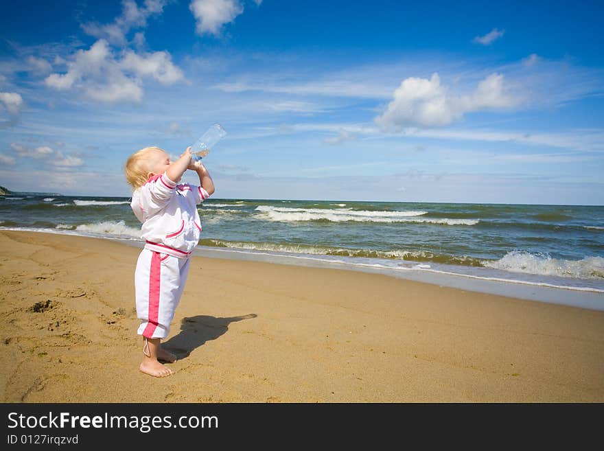 Little girl standing on coastline and drinking water. Little girl standing on coastline and drinking water