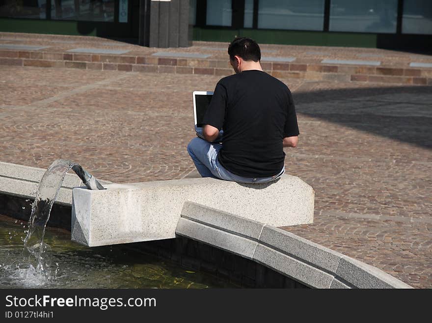 Man with a pc nearby a fountain