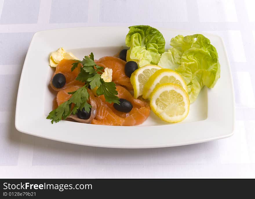 Salty salmon decorated with salad leaves, lemon slice, olives and parsley on white plate