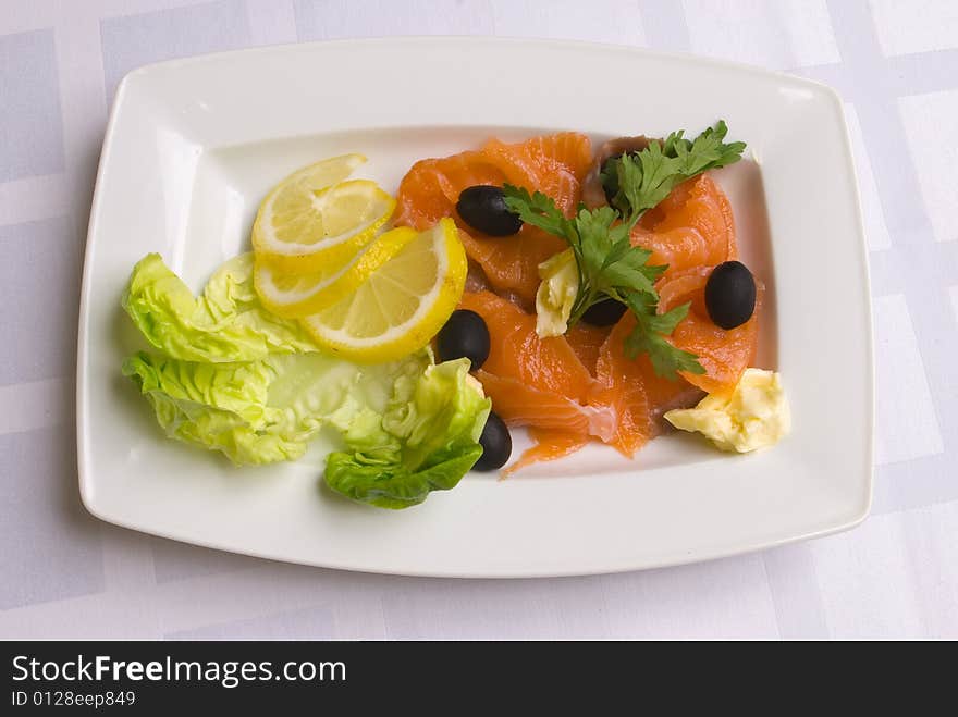 Salty salmon decorated with salad leaves, lemon slice, olives and parsley on white plate