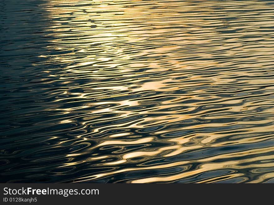 Warm golden tones of a sun reflected on the ripples of a sea surface. Warm golden tones of a sun reflected on the ripples of a sea surface