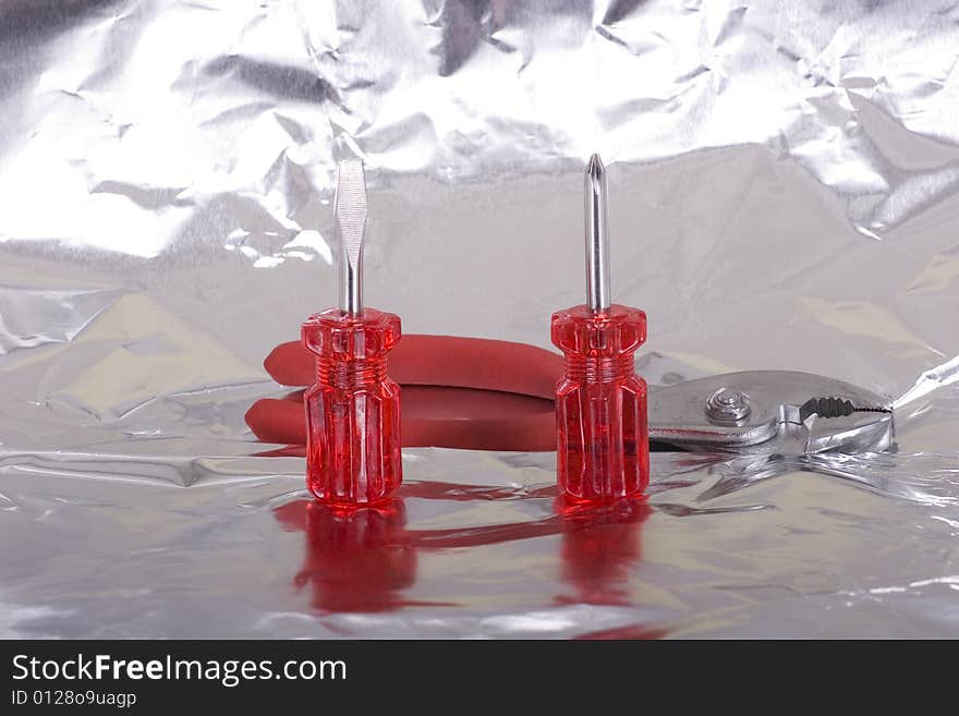 Two screwdrivers and a pair of pliers on a reflective surface. Two screwdrivers and a pair of pliers on a reflective surface